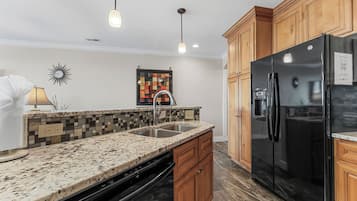 Una cocina con encimeras de granito, armarios de madera, refrigerador negro e iluminación colgante.