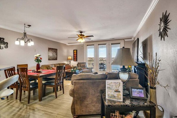 A spacious living room with a dining area, a ceiling fan, and a large window providing a view of the outdoors.
