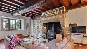 Una sala de estar acogedora con chimenea de piedra, un sofá, un televisor y un ventanal grande.