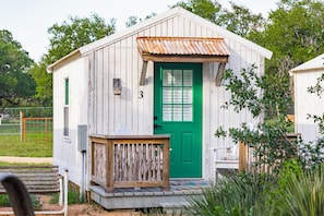 Une petite cabane en bois avec une porte verte, portant le numéro 3, et un banc en bois à l’extérieur.