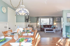 Un coin repas avec une table en bois dressée pour le repas, un lustre et un salon avec un canapé et un téléviseur.