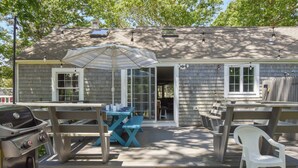A house with a patio area featuring a grill, a table with chairs, and an umbrella. - Peace and Quiet & Spacious Back Deck (Wellfleet)