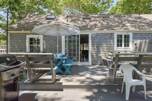 Une maison dotée d’un patio comprenant un barbecue, une table avec des chaises et un parasol.