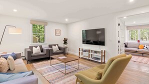 A modern living room with a flat-screen TV, two sofas, a coffee table, and a bookshelf.