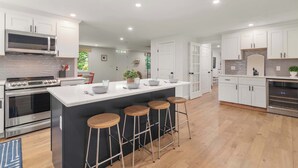 A modern kitchen with a central island, bar stools, stainless steel appliances, and white cabinetry. - Heated In-Ground Pool and New Central AC! (Brewster)