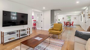 A modern living room with a flat-screen TV, a yellow armchair, a wooden coffee table, and a sofa.