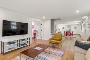 A modern living room with a flat-screen TV, a yellow armchair, a wooden coffee table, and a sofa.