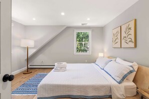 A bedroom with a bed, a window, a floor lamp, and a wall with framed artwork. - Heated In-Ground Pool and New Central AC! (Brewster)