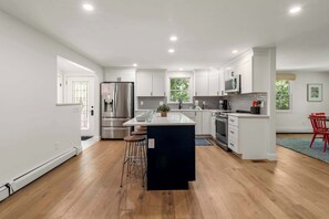 A modern kitchen with white cabinetry, stainless steel appliances, and a central island with stools. - Heated In-Ground Pool and New Central AC! (Brewster)