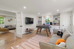 A modern living room with a sofa, a coffee table, a television, and a foosball table.