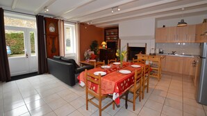 A dining area with a table set for four, a sofa, a fireplace, and a kitchen with wooden cabinets. - Le Clos Neuf - SAINT-GUINOUX (SAINT-GUINOUX)