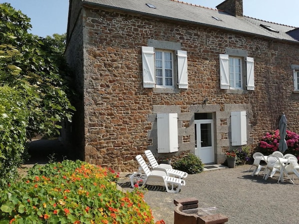 A stone building with a gravel driveway, white shutters, and outdoor seating.