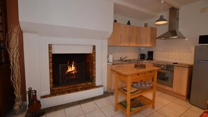 A kitchen with a brick fireplace, wooden cabinets, a wooden table, and a stainless steel refrigerator. - Le Clos Neuf - SAINT-GUINOUX (SAINT-GUINOUX)
