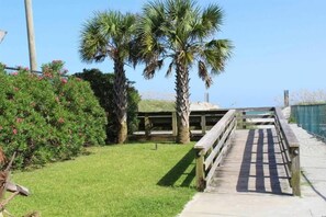 A wooden boardwalk leading to a building with a sloped roof, surrounded by palm trees and green shrubs. - Lovely 2BR,Pool,M28 (Myrtle Beach)