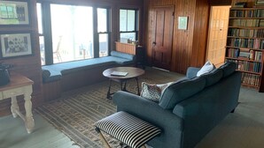 Un salon chaleureux avec un canapé bleu, une table basse ronde et un tapis à motifs. On y trouve une bibliothèque remplie de livres et une porte en bois.