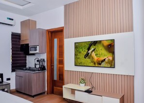 Eine moderne Küche mit integriertem Mikrowellenherd, Herd und Kaffeeautomat, einer Holztür sowie einem an der Wand montierten Fernseher.