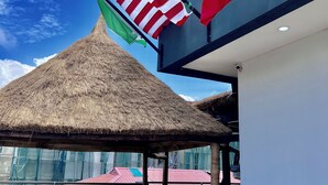 Eine Terrasse mit einem Reetdach, Gartenmöbeln, einem Grill und den Flaggen der USA und Kanadas.