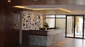 A reception area with a wooden ceiling, a decorative wall with leaf patterns, a reception desk with a patterned base, and a view of the outdoors through glass doors. - Rumah Highlands Hotel (Cebu)