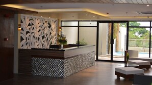 A reception area with a modern design, featuring a reception desk, a decorative wall, and a view of the outdoors. - Rumah Highlands Hotel (Cebu)