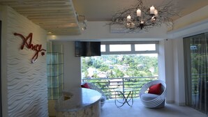 A modern interior with a curved stone counter, a chandelier, and a balcony with a view of a residential area. - Rumah Highlands Hotel (Cebu)