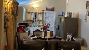 Een woonkamer met een bruine leren bank, een eettafel met stoelen en een keuken in de achtergrond.