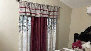Een slaapkamer met een bed, gordijnen, een hoofdbord en een vloerkleed.