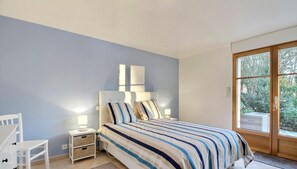 A bedroom with a bed, bedside table, lamp, and a view of the outdoors through a door. - At Lolita and Robert's (BADEN)
