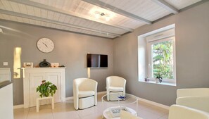 A modern living room with a fireplace, white furniture, a clock, and a TV. - At Lolita and Robert's (BADEN)