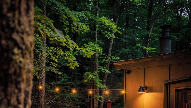 An outdoor deck with a table and chairs, surrounded by trees and a wood-burning stove.