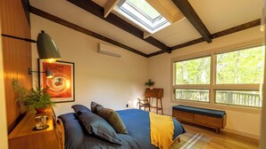 A bedroom with a bed, a bench, a skylight, a window, and a plant.