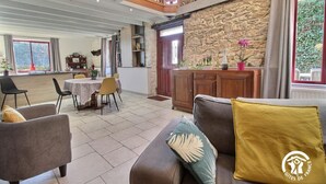 Amplia sala de estar con techo alto, pared de piedra, mesa de comedor con sillas y sofá con cojines.