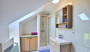 A modern bathroom with a shower, a sink, and a vanity. There is a towel rack and a small shelf with toiletries. - Casa Camélias - LIMERZEL (LIMERZEL)