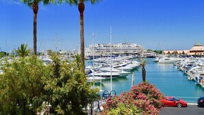 Un port de plaisance où sont amarrés de nombreux bateaux, des palmiers et, au fond, un bâtiment à la façade blanche.