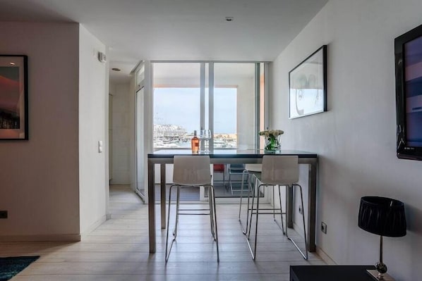 A modern kitchen with a large window, two bar stools, and a dining table.