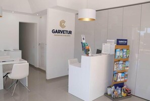 Un espace d’accueil comprenant un bureau blanc, une chaise blanche, un comptoir d’accueil et une bibliothèque contenant des brochures.