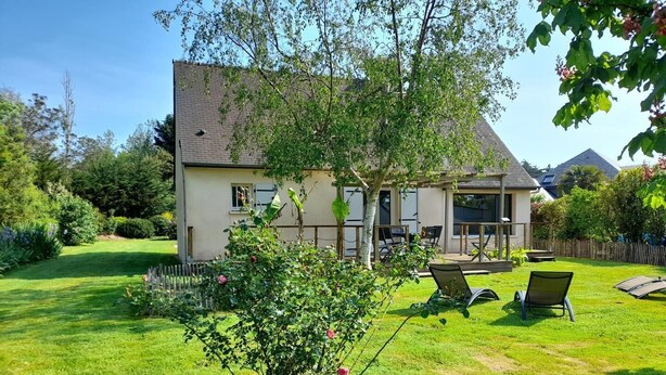 Een huis met een ruime achtertuin, een terras met tuinmeubilair en een kleine tuin met een rozenstruik.