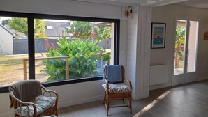 Een ruime kamer met grote ramen, rieten stoelen en uitzicht op een tuin.