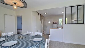 Een eethoek met een tafel voor vier personen, een keuken met een koelkast, en een trap naar een hoger niveau.