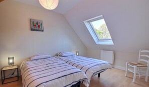 A bedroom with two beds, a skylight, a white chair, and a nightstand with a lamp. - Kerbana - Sarzeau - Gîte (SARZEAU)