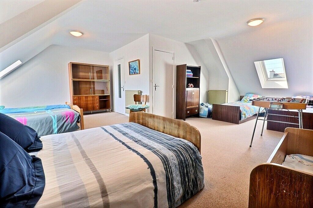 A spacious attic bedroom with two beds, a desk, and a wardrobe.