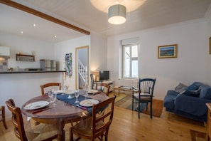 Un comedor con una mesa de madera dispuesta para cuatro personas, un sofá azul y una cocina al fondo.