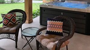 A covered patio area with a hot tub, wicker chairs, and a glass table. - Bright & Clean Chalet with Hot Tub (Acme)
