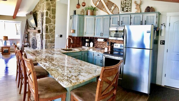 A kitchen with a granite countertop, blue cabinets, a stainless steel refrigerator, and a stone wall. - Bright & Clean Chalet with Hot Tub (Acme)