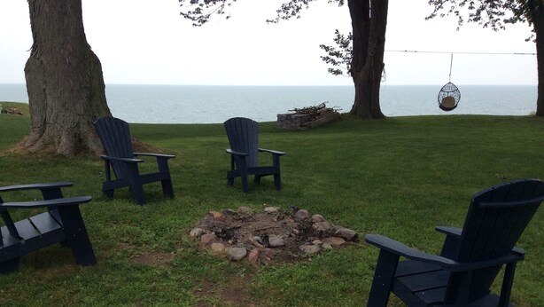 Un espace extérieur verdoyant avec un foyer, plusieurs fauteuils Adirondack et une balançoire suspendue.