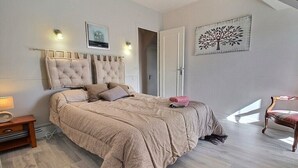 Un dormitorio con una cama grande, una mesita de noche, una silla y una puerta que da a otra habitación.