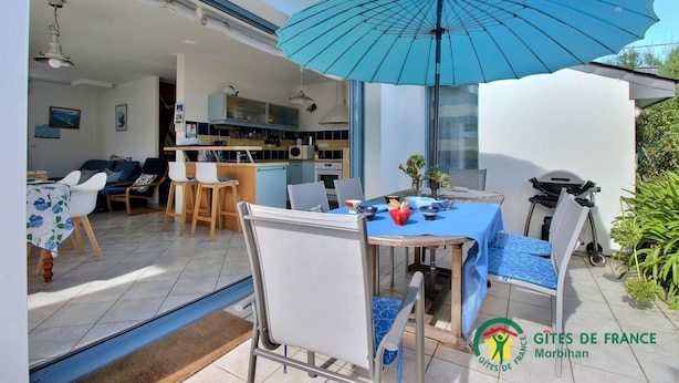 Une cuisine moderne avec un coin repas, un parasol bleu et une vue sur l’extérieur.