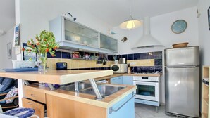 Une cuisine moderne équipée d’une cuisinière, d’un four et d’un réfrigérateur intégrés. On y trouve un évier avec un robinet, une fenêtre au-dessus de l’évier et un luminaire suspendu.