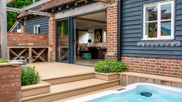 A modern house with a hot tub, wooden deck, and brick walls.