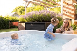 En familj i ett bubbelbad med en trädgård och en byggnad i tegel som syns i bakgrunden.
