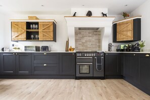 Eine moderne Küche mit schwarzen Schränken, einem eingebauten Backofen und Holzregalen.
